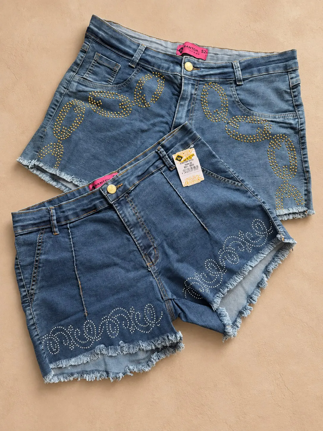 Shorts jeans Plus com aplicações metálicas e barras desfiadas.