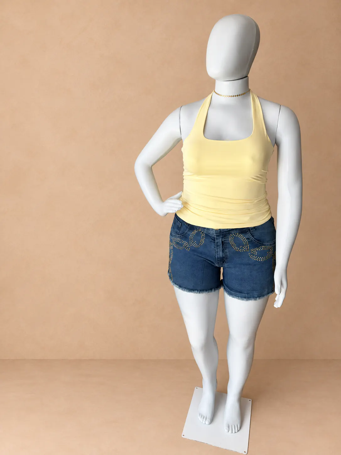 Look Plus com blusa amarela frente única e short jeans com aplicações douradas.